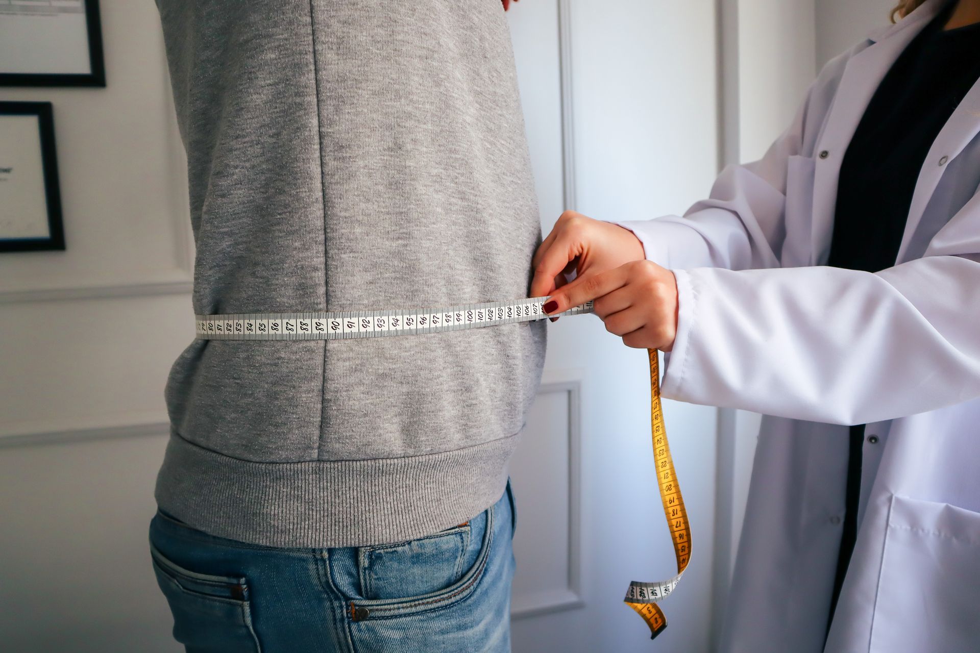 A clinician measuring a patient's waist with a tape measure during an assessment